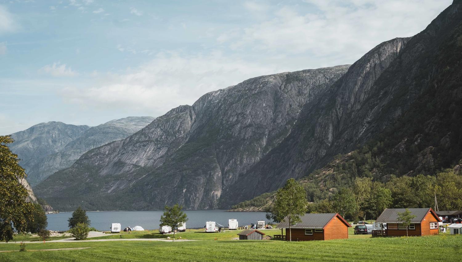 Sæbø camping sett fra hovedveien, med vann og fjell i bakgrunnen.