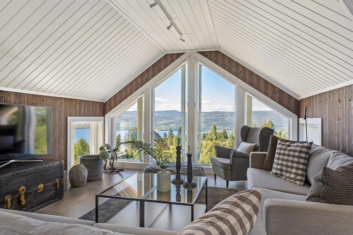 En lys stue med store vinduer og utsikt over landskapet utenfor.