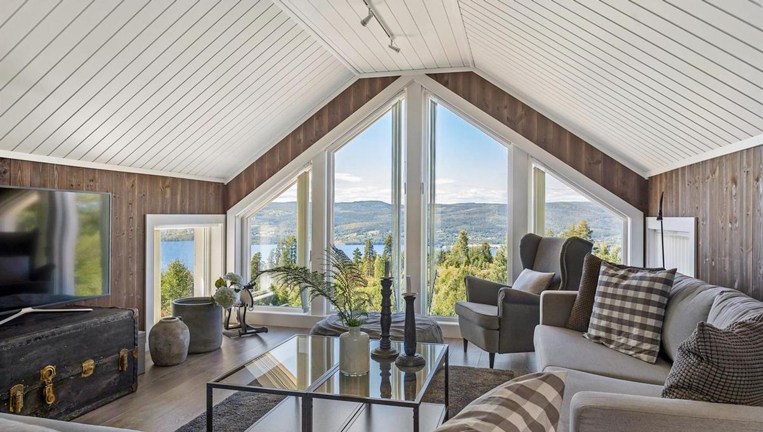 En lys stue med store vinduer og utsikt over landskapet utenfor.