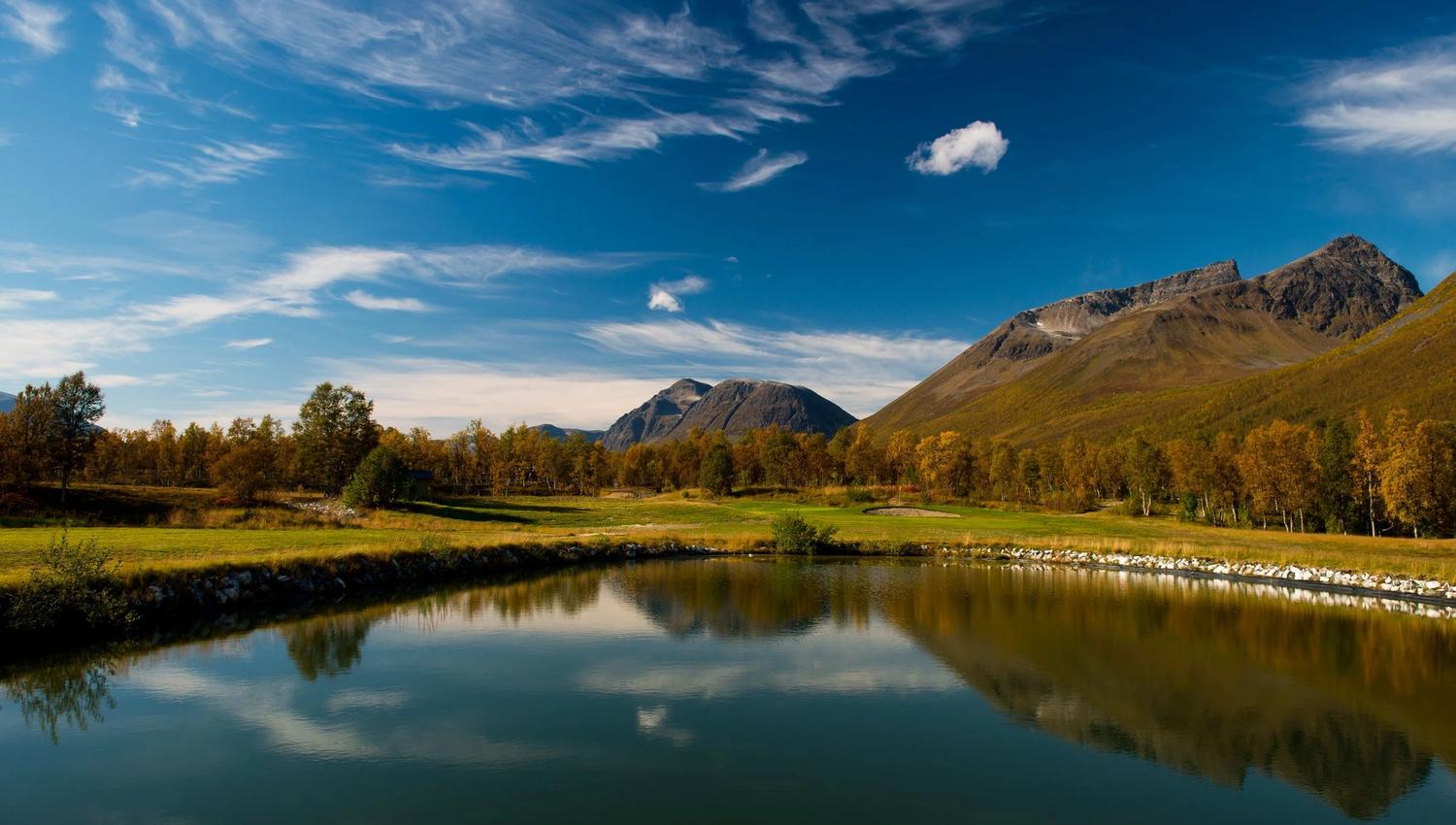 Mountain landscape with a lake, autumn-coloured trees, and a clear sky.