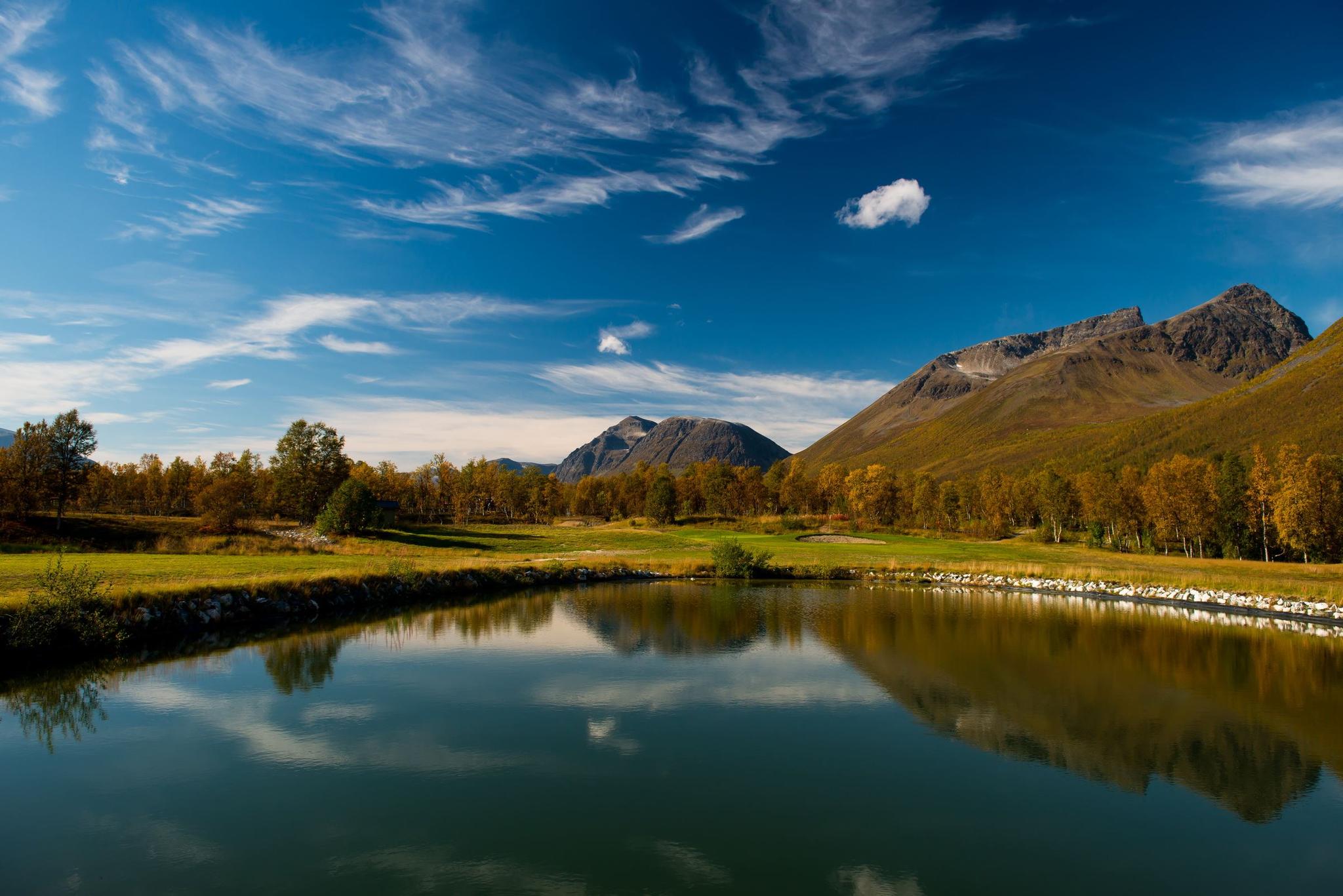Mountain landscape with a lake, autumn-coloured trees, and a clear sky.