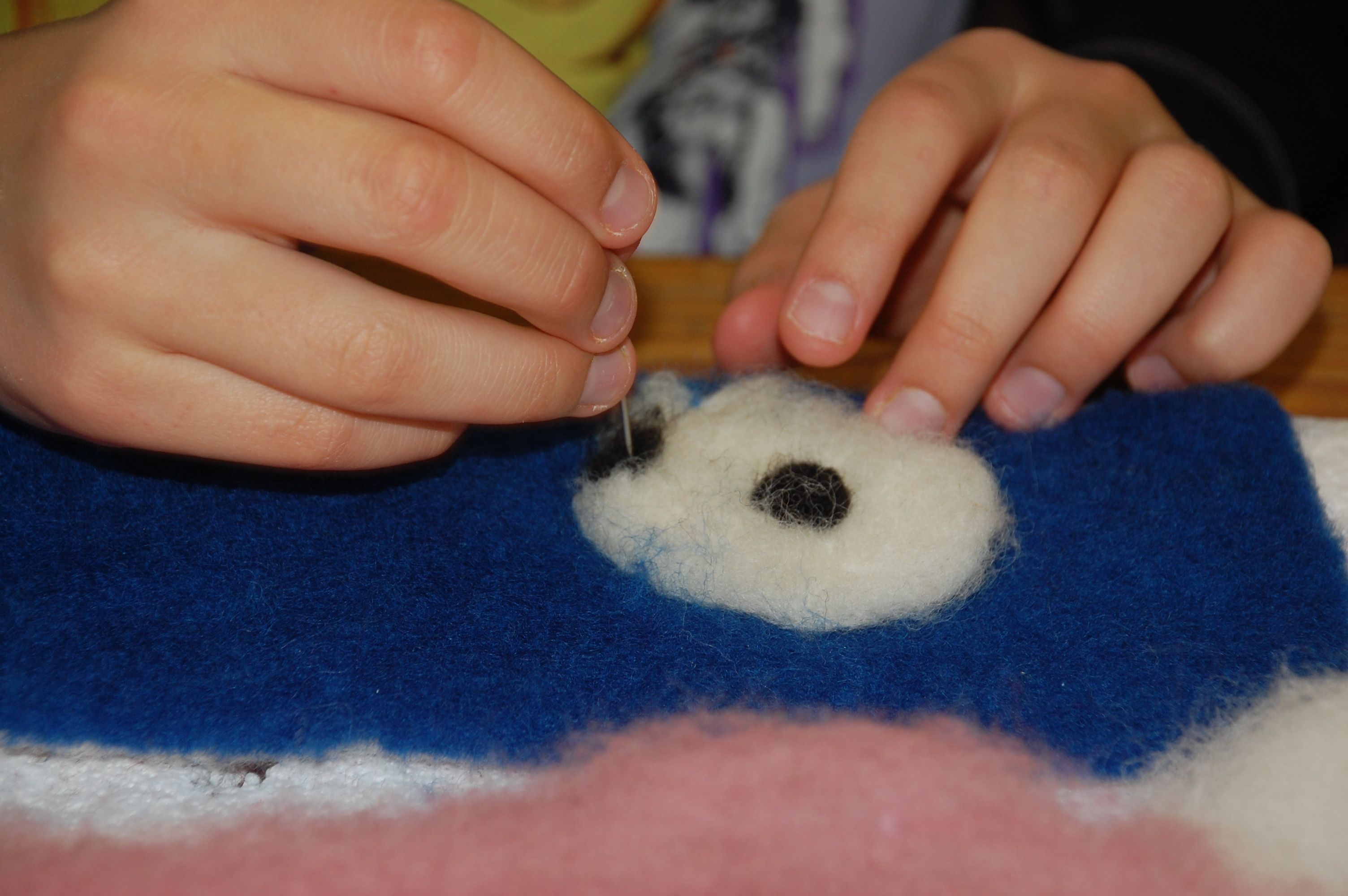 Two hands with a needle, placed on wool and felt.
