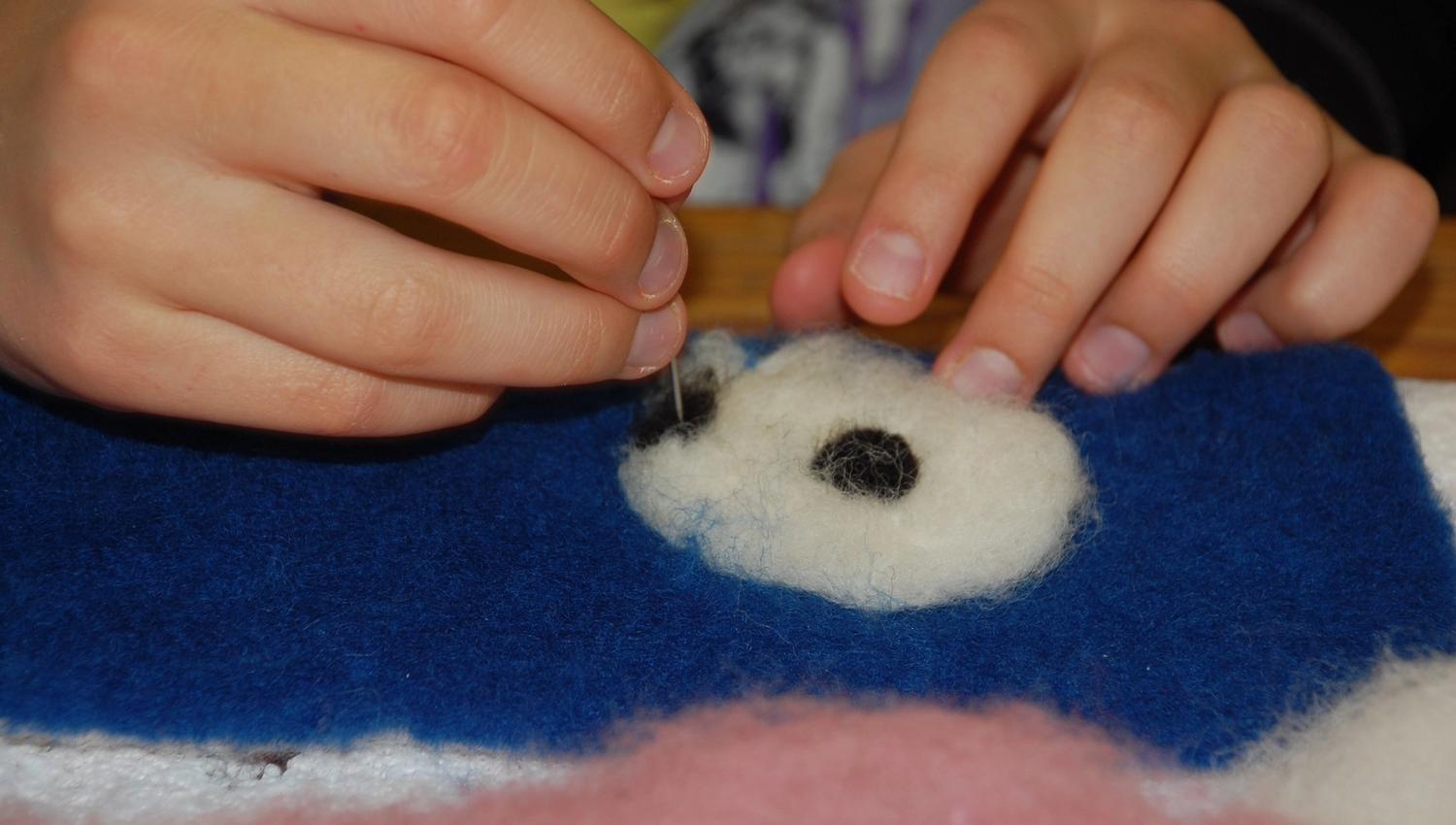 Two hands with a needle, placed on wool and felt.