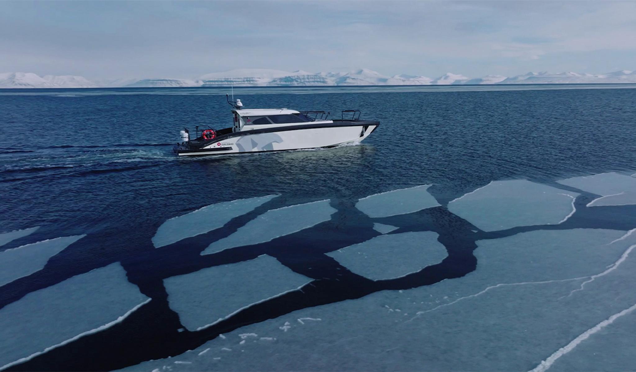 A boat sailing along sheets of ice floating on a fjord, with snow-covered mountains far away in the background