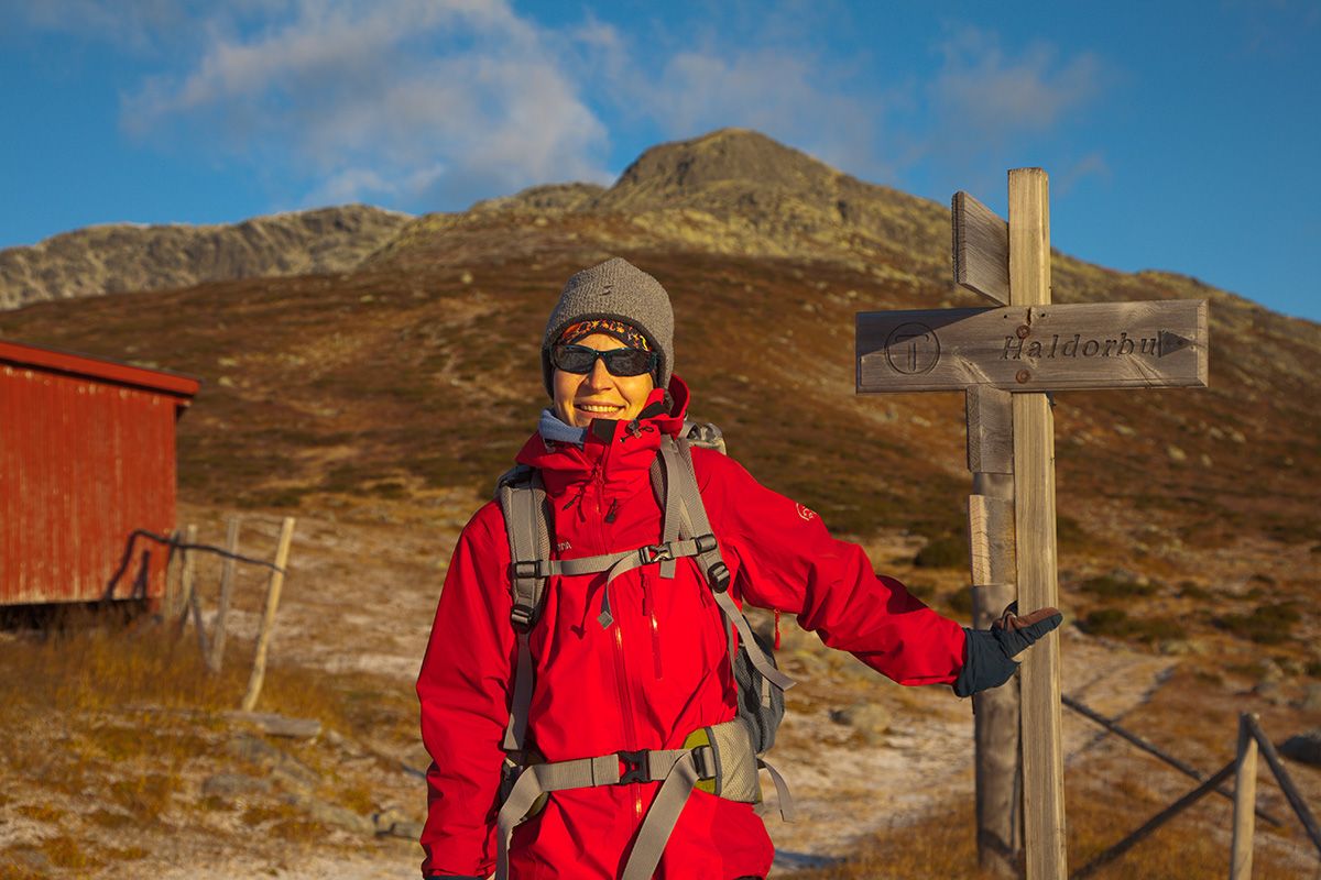 Hiker in a red jacket outside the cabin Storeskag at the sign pointing the way towards the summit of Skaget.
