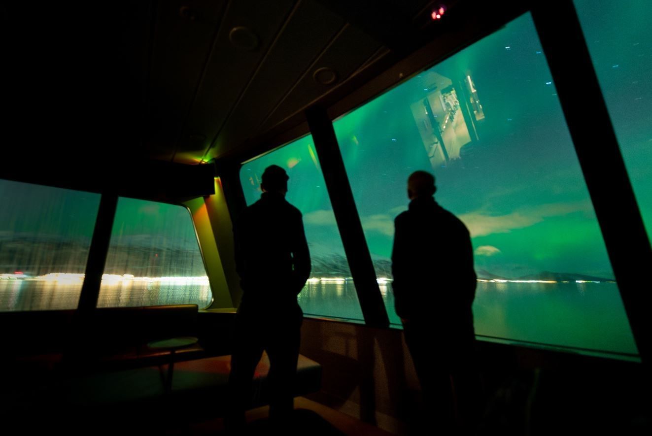 Two people viewing the Northern Lights from inside the boat