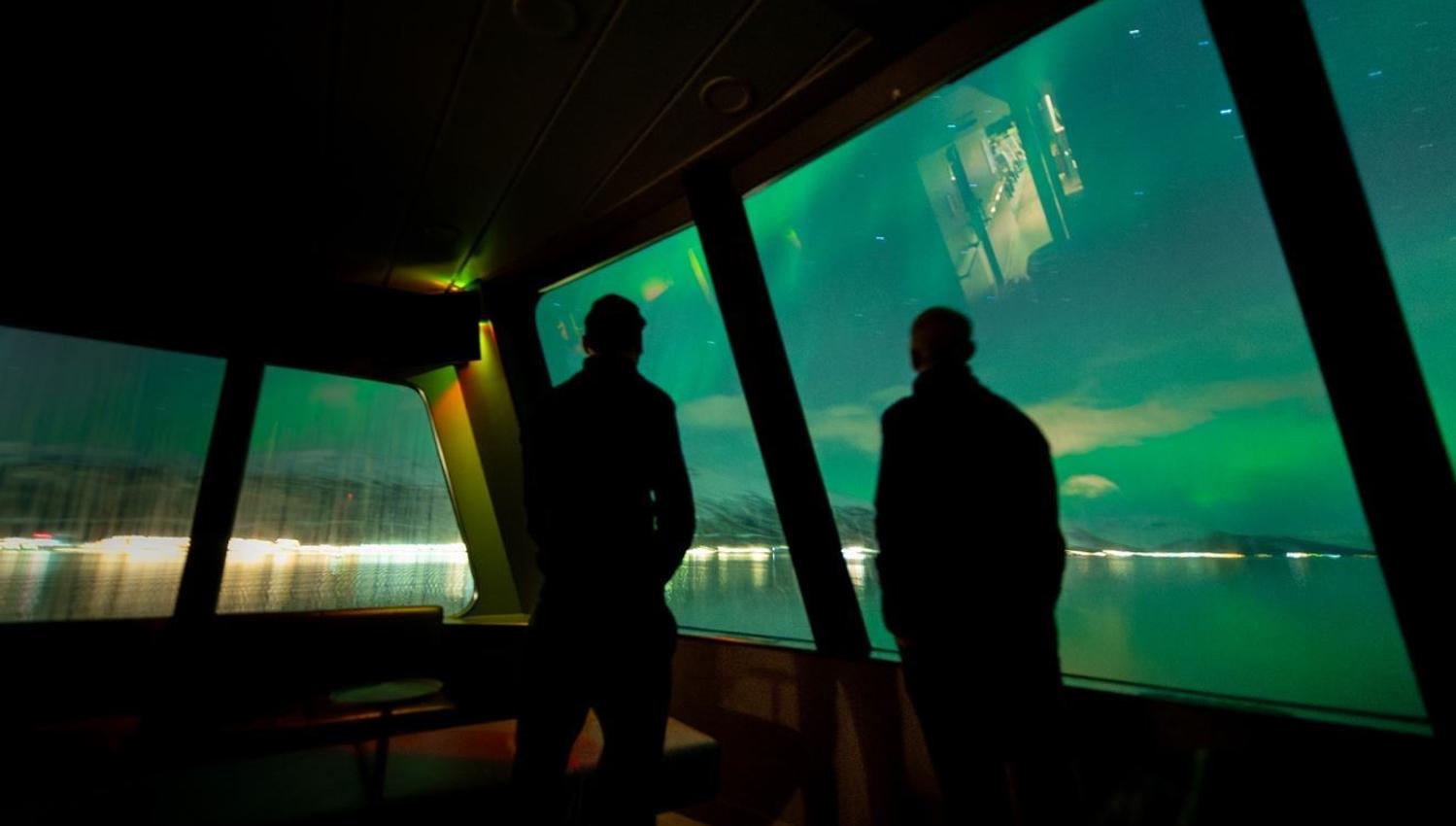 Two people viewing the Northern Lights from inside the boat