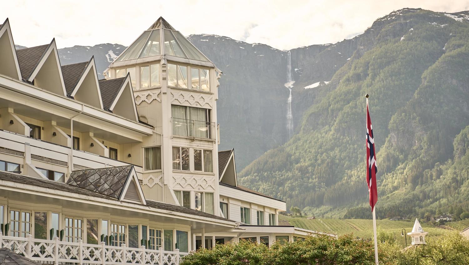 Det ikoniske tårnet på Hotel Ullensvang med fossefall i fjellsida som bakteppe.