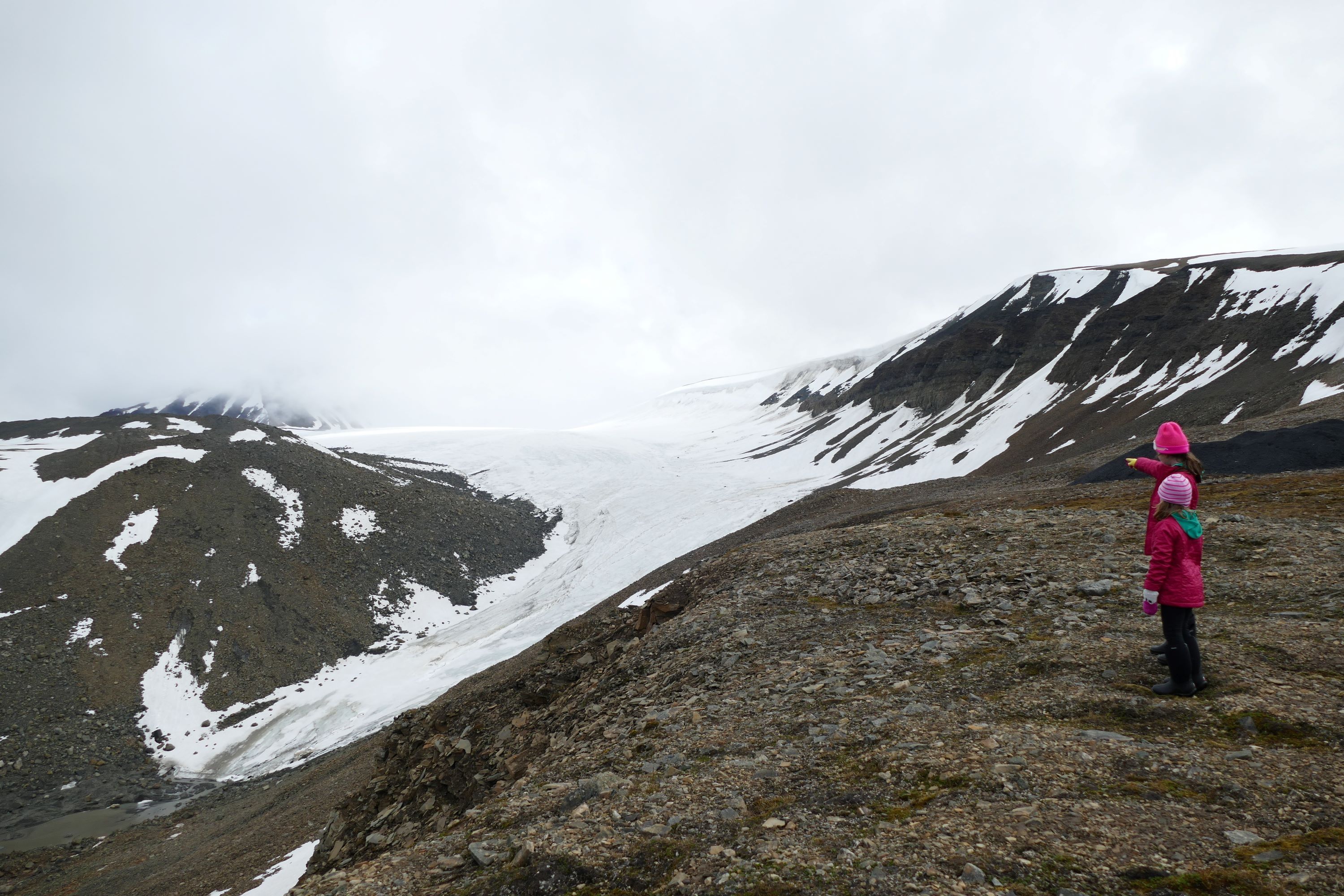 Two small people pointing at a snow covered valley with a mountin in the background