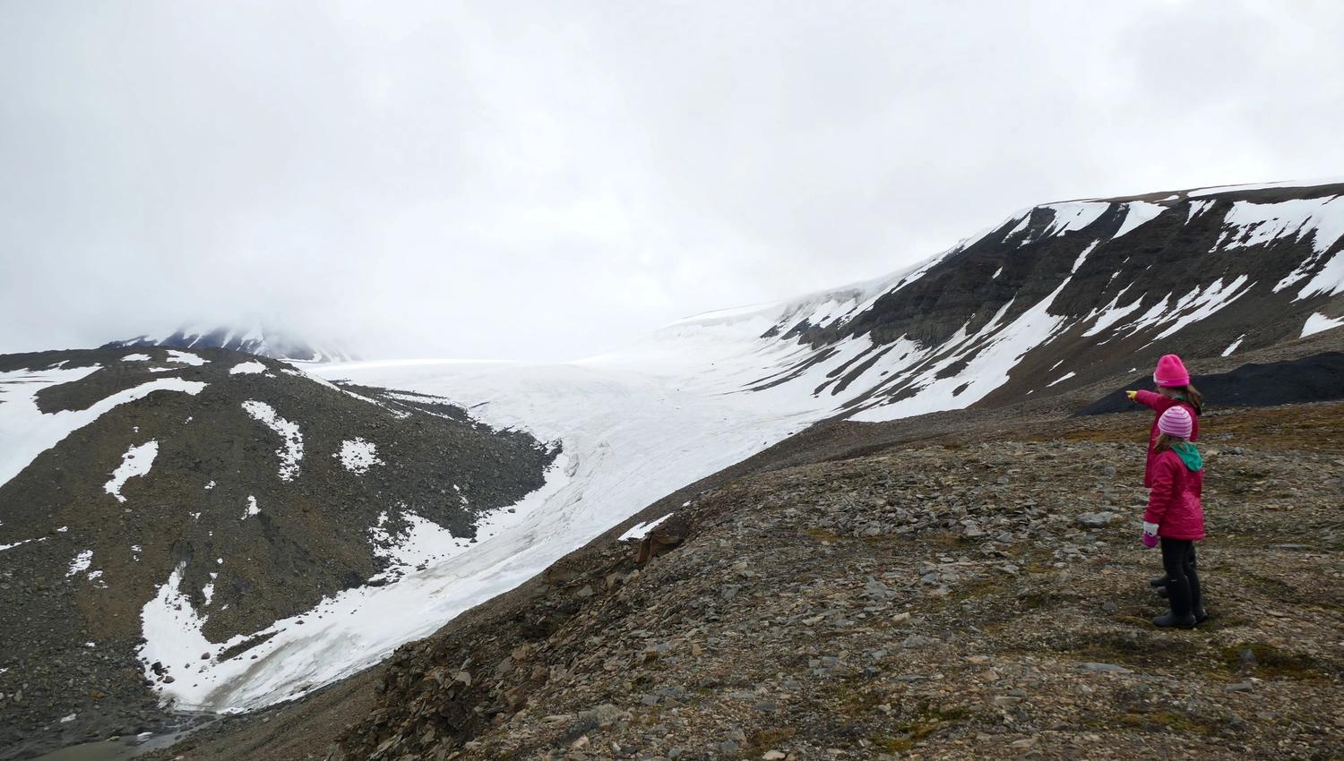 Two small people pointing at a snow covered valley with a mountin in the background