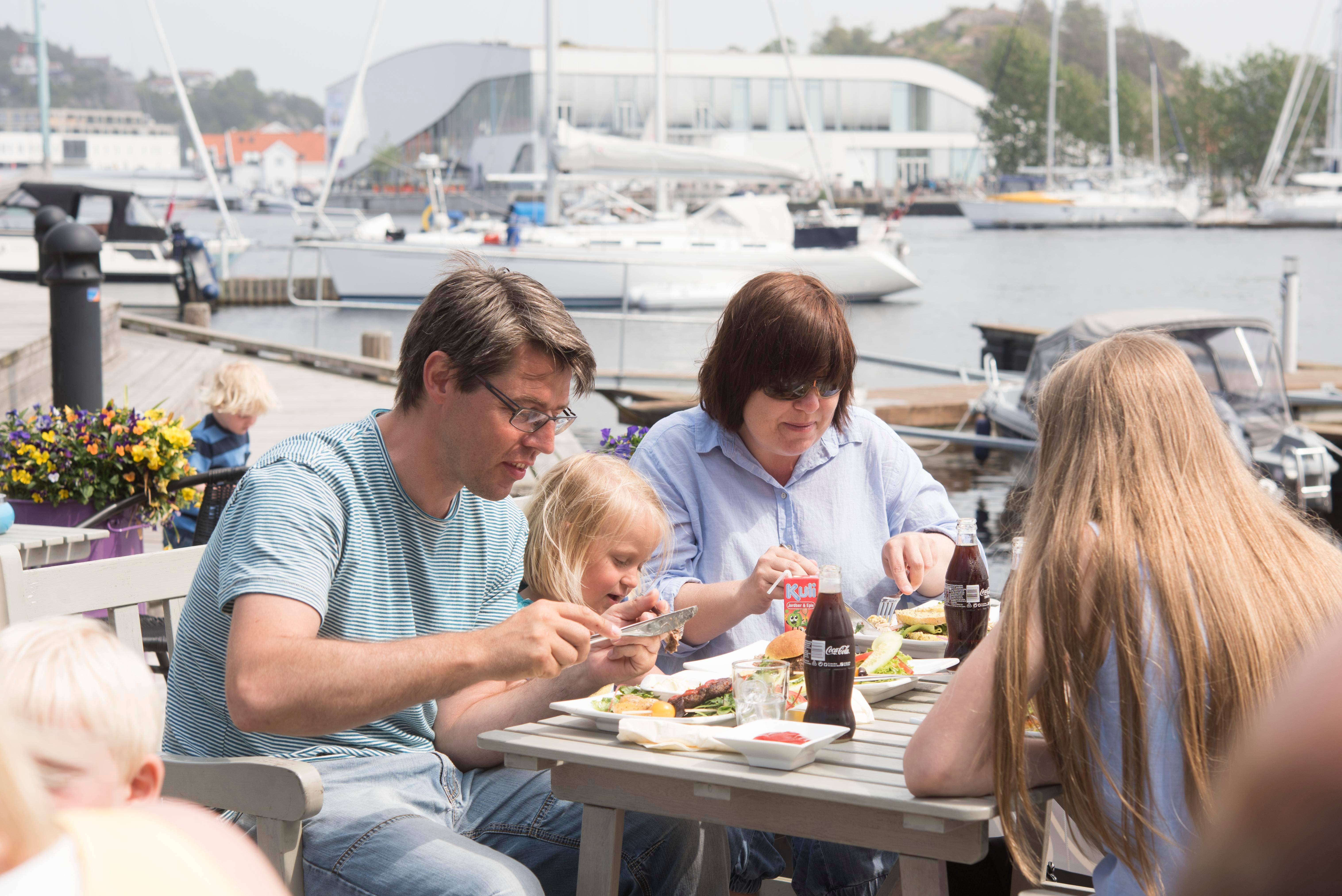 Family of four sitting outside, enjoying good food and drinking cola from glass bottles.