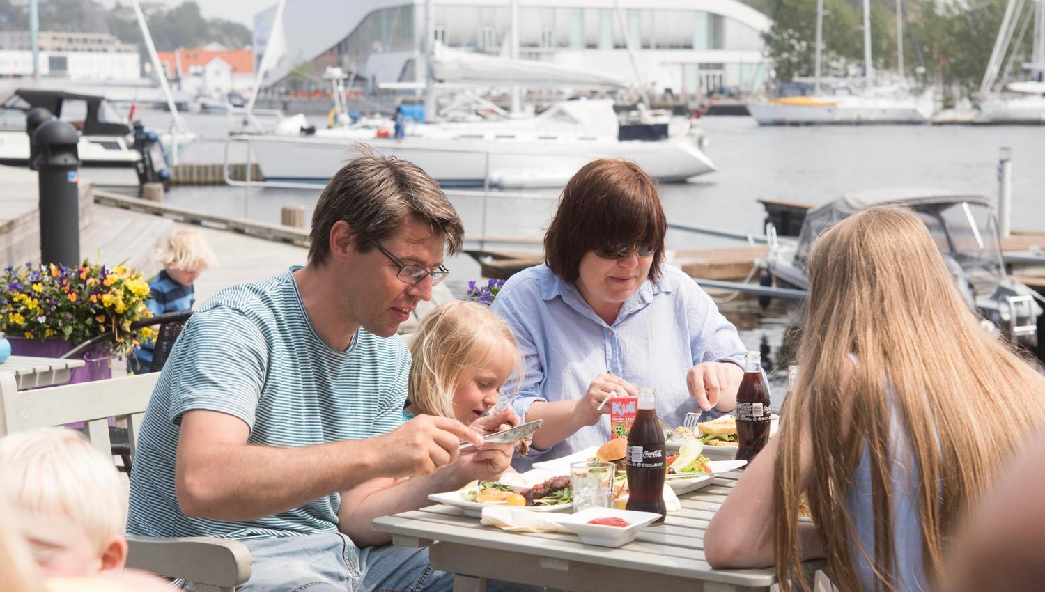 Family of four sitting outside, enjoying good food and drinking cola from glass bottles.