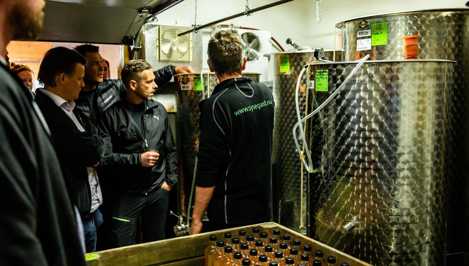 Gruppe med besøkande får ei omsyning i siderproduksjon hos ein lokal produsent i Ulvik.