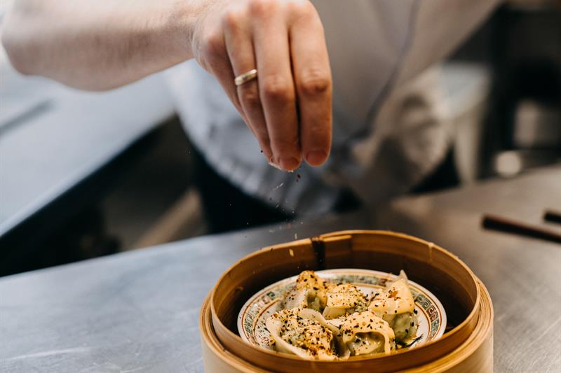 A cook is sprinkling seasoning over an Asian dish