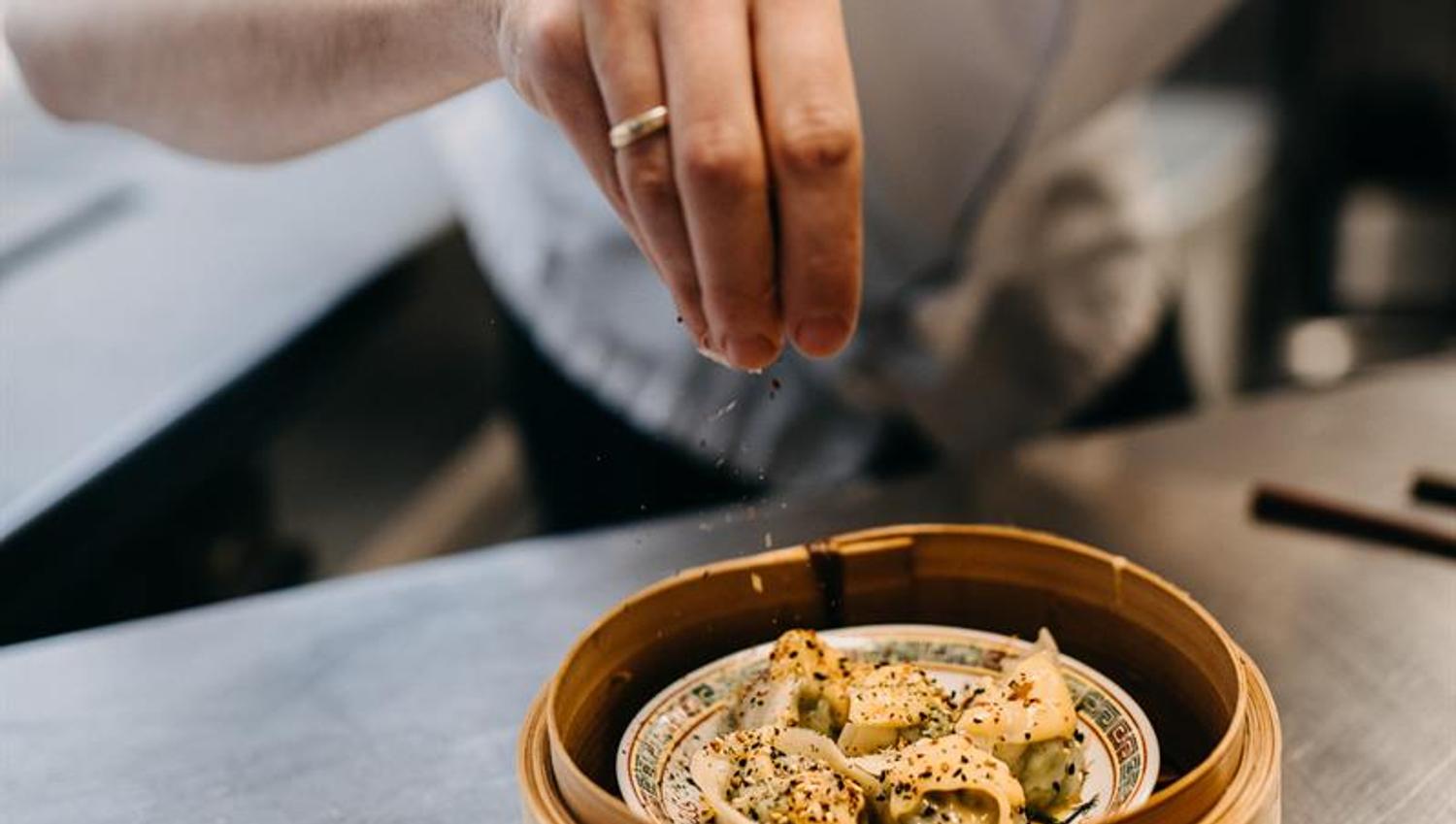 A cook is sprinkling seasoning over an Asian dish
