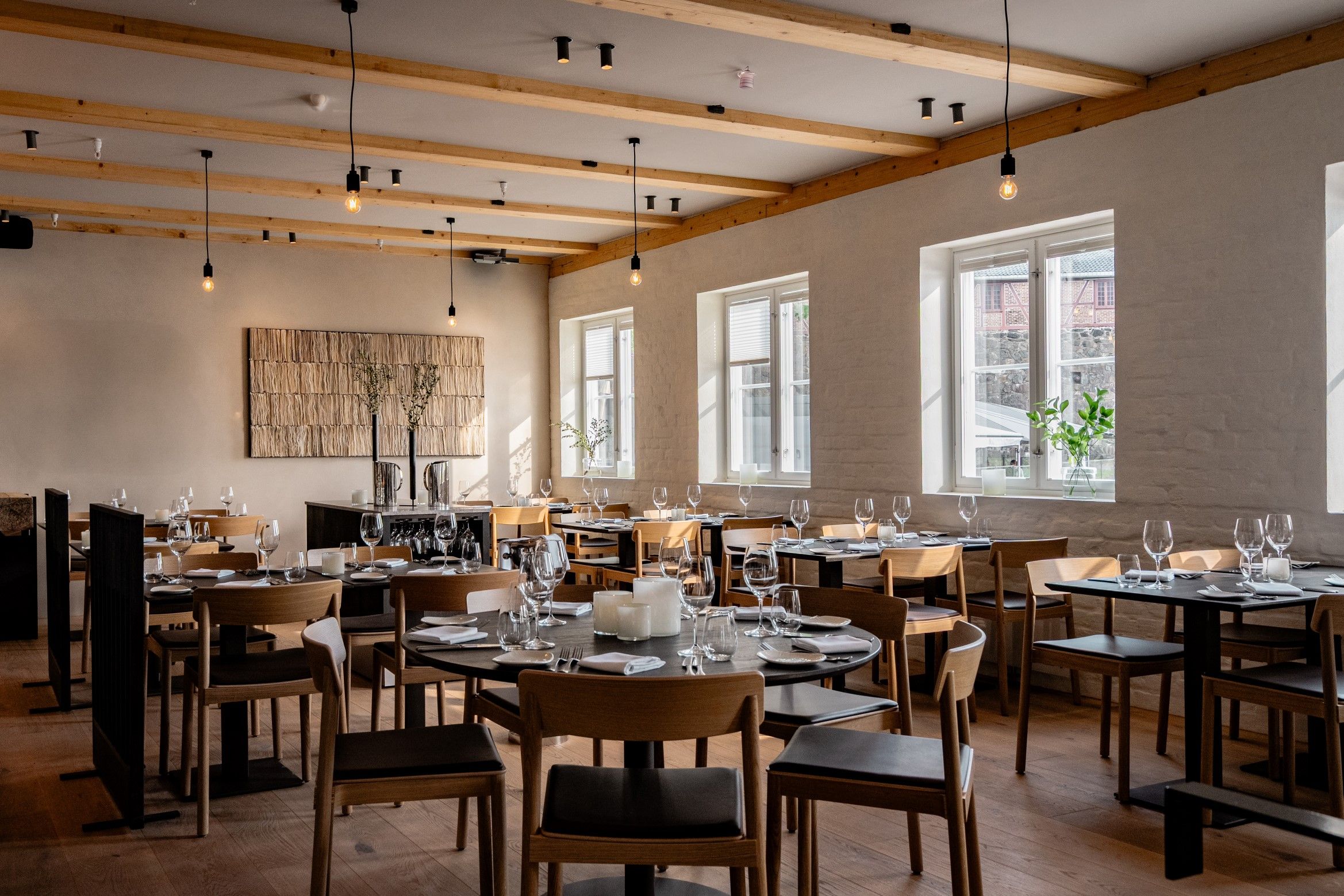 Restaurantineriør med sorte bord og lyse stoler, og lyspærer hengende ned fra taket