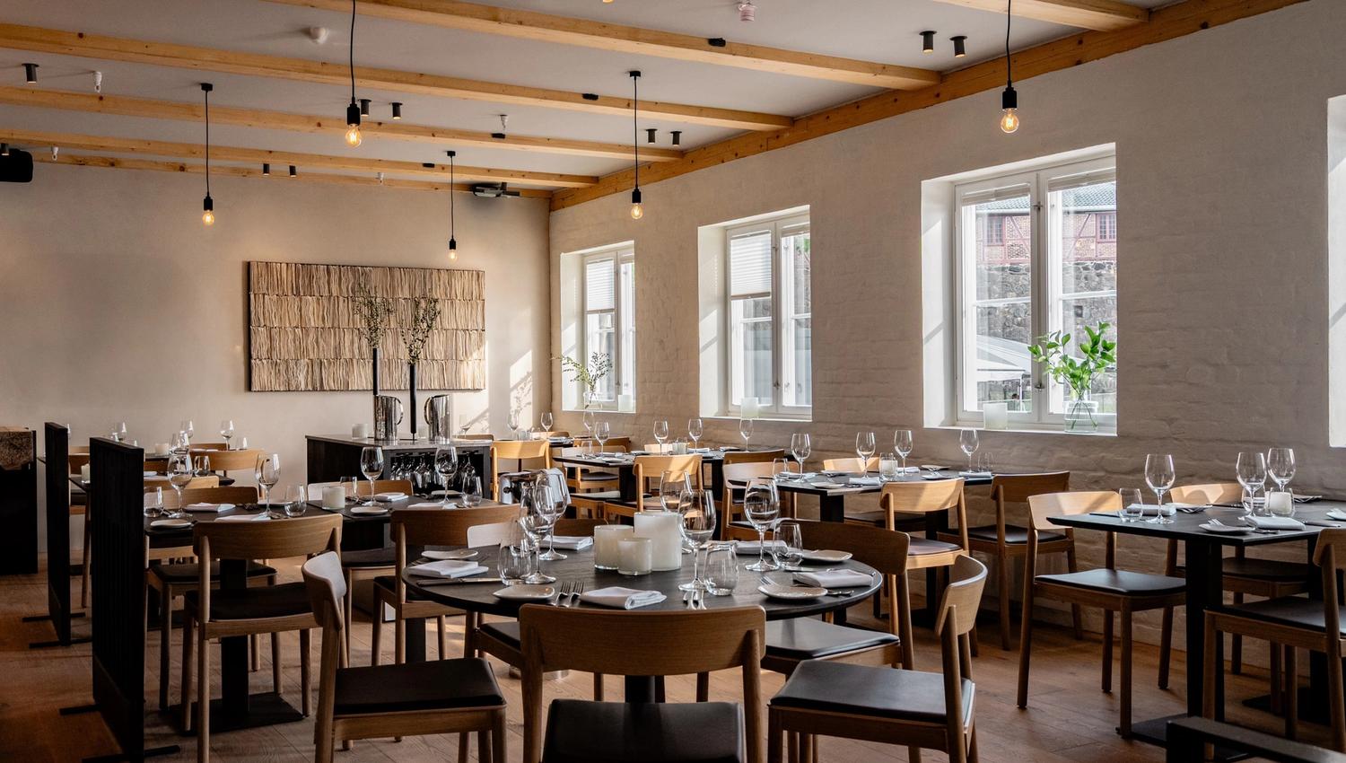 Restaurantineriør med sorte bord og lyse stoler, og lyspærer hengende ned fra taket