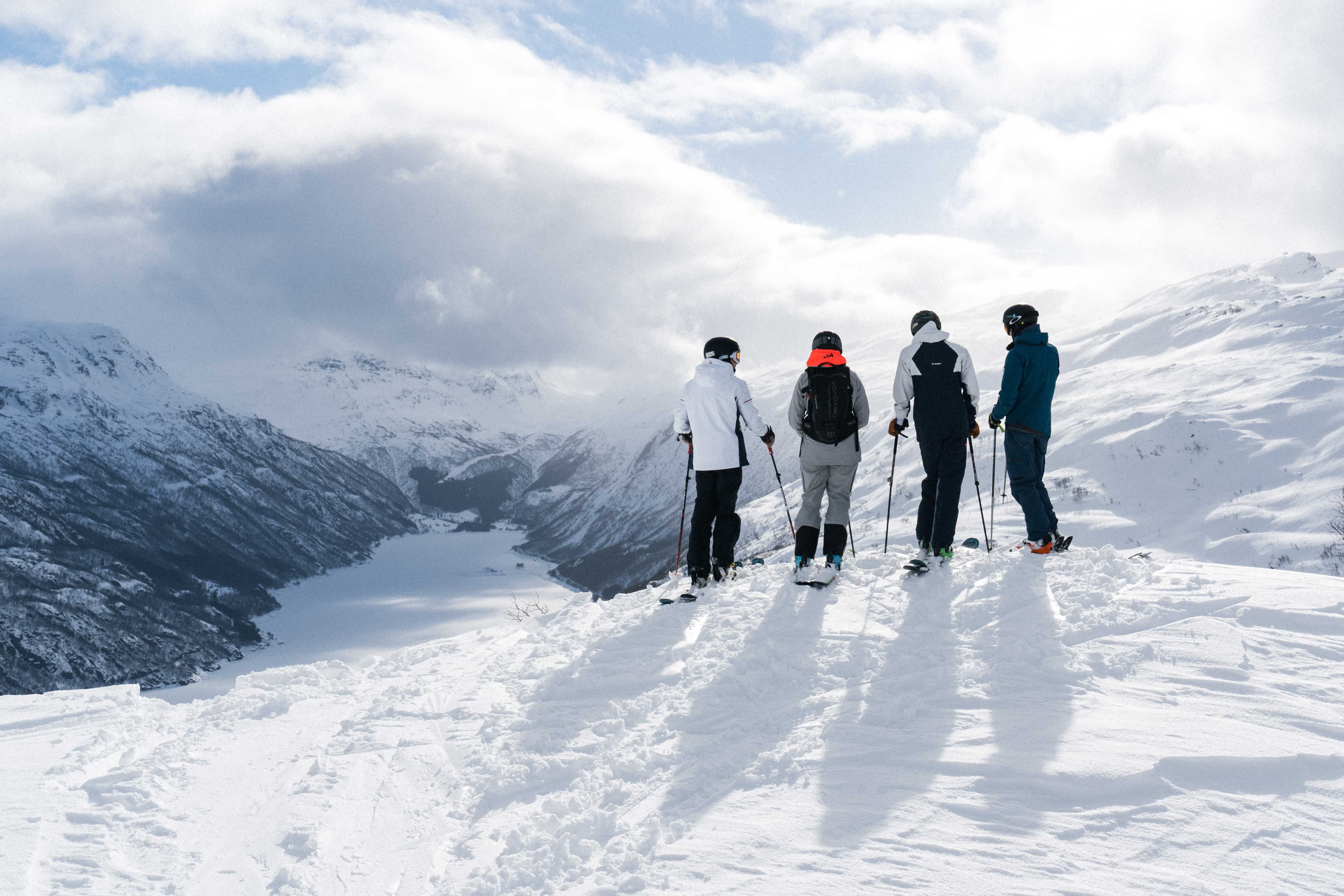 Fire personer på slalomski står og ser utover et snøkledd landskap.