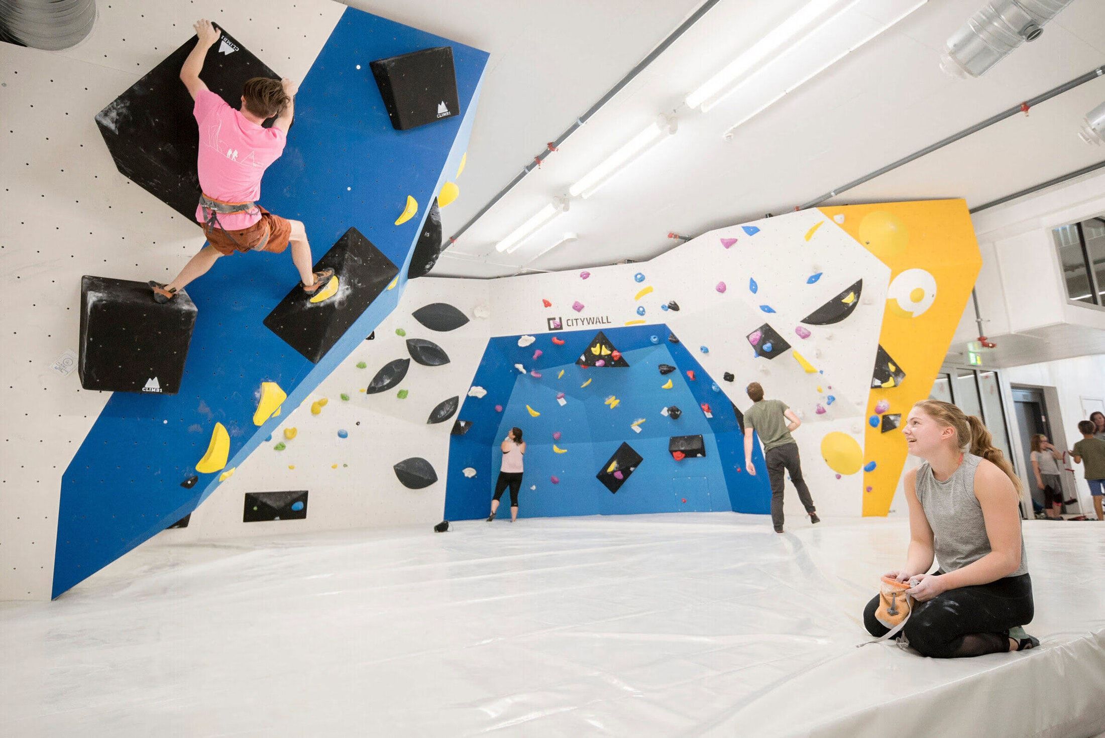 People bouldering in an indoor climbing gym with colourful holds and padded mats.
