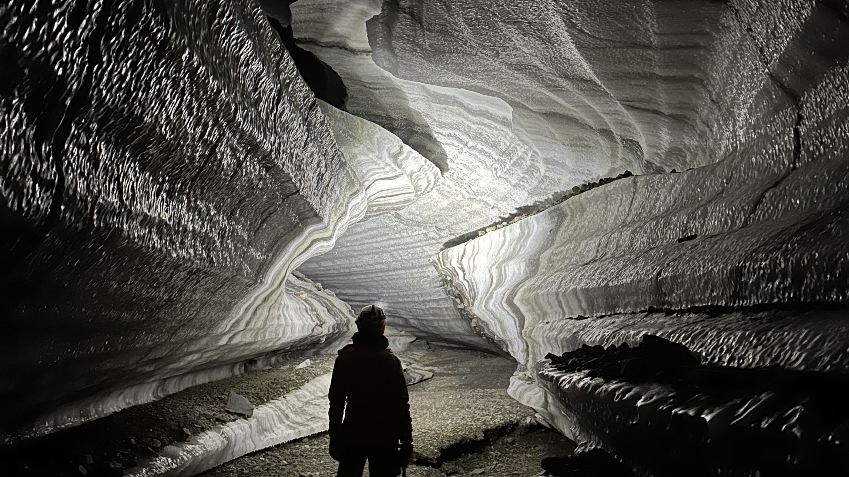 Person standing inside an ice cave with a head lamp