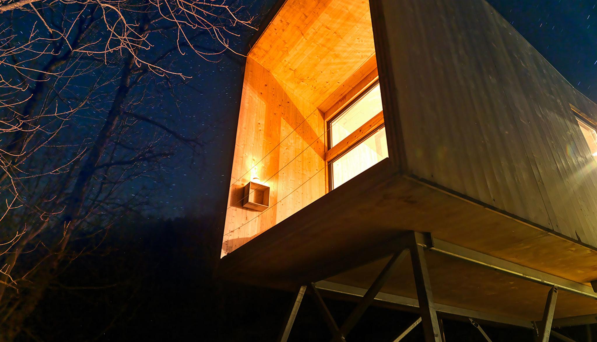 Modern cabin on stilts by the fjord in Hardanger, illuminated in the evening darkness.