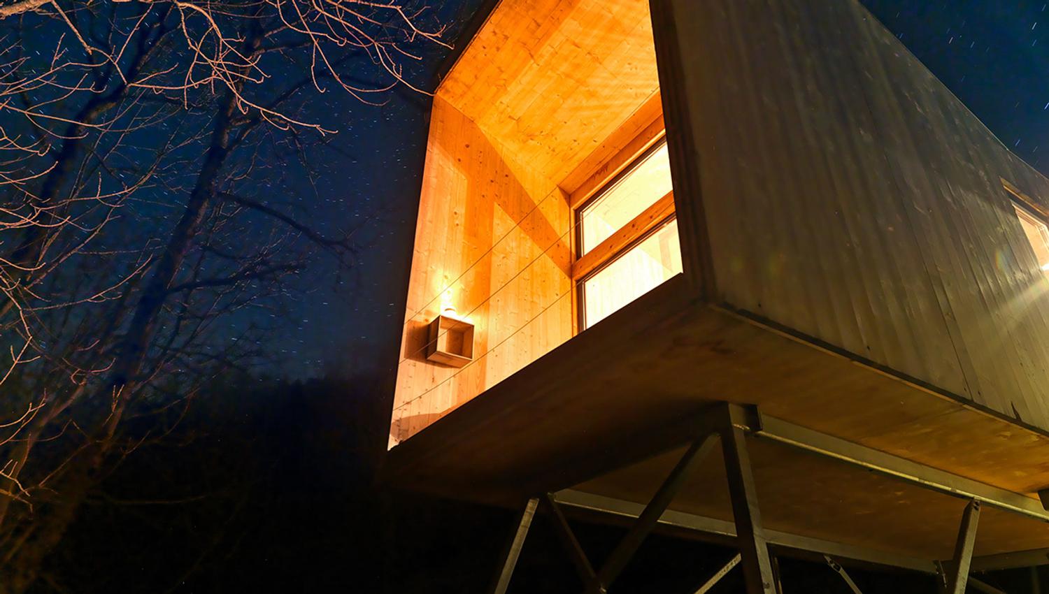 Modern cabin on stilts by the fjord in Hardanger, illuminated in the evening darkness.