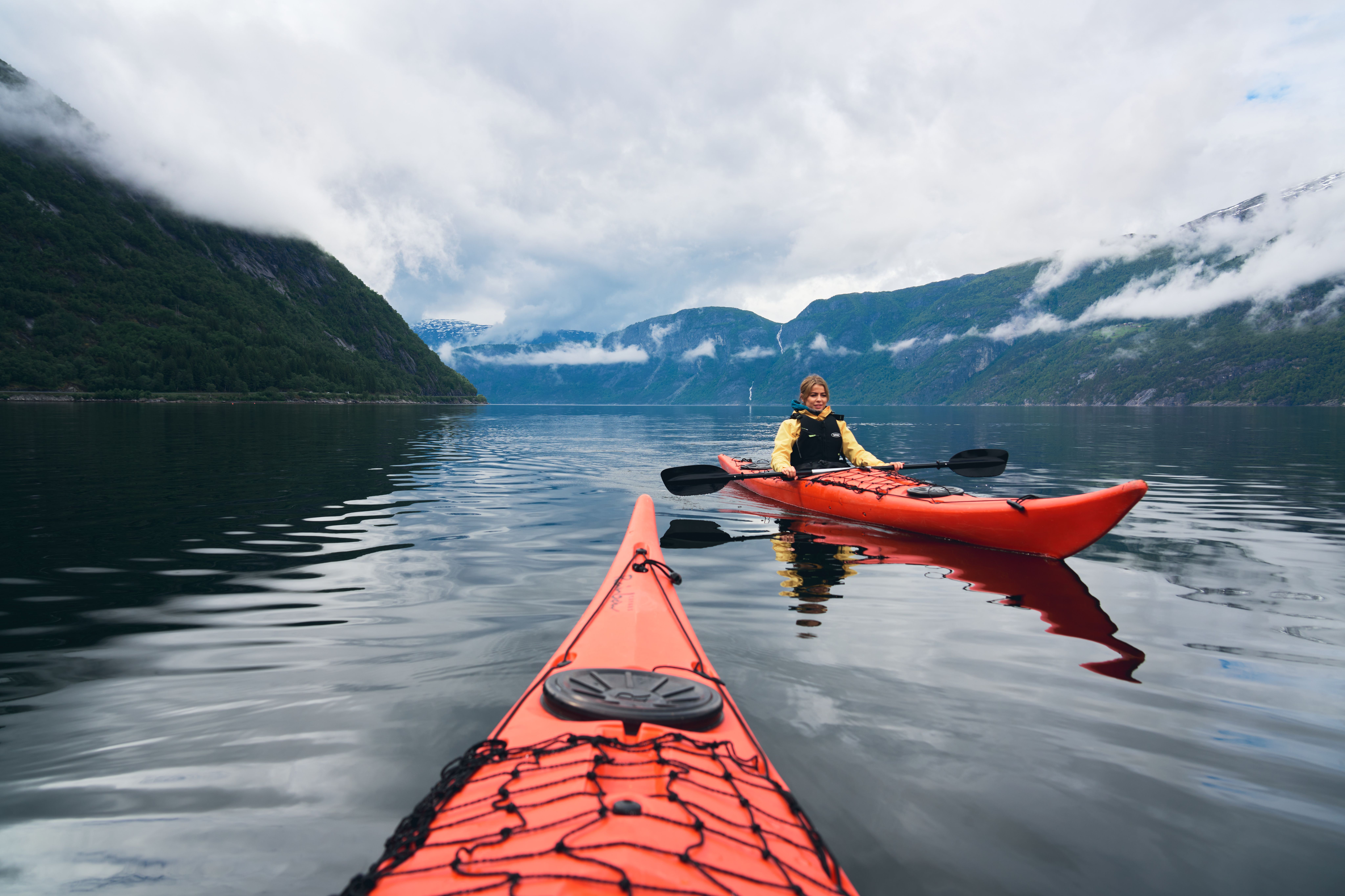 A woman in a red kayak with misty mountains in the background.