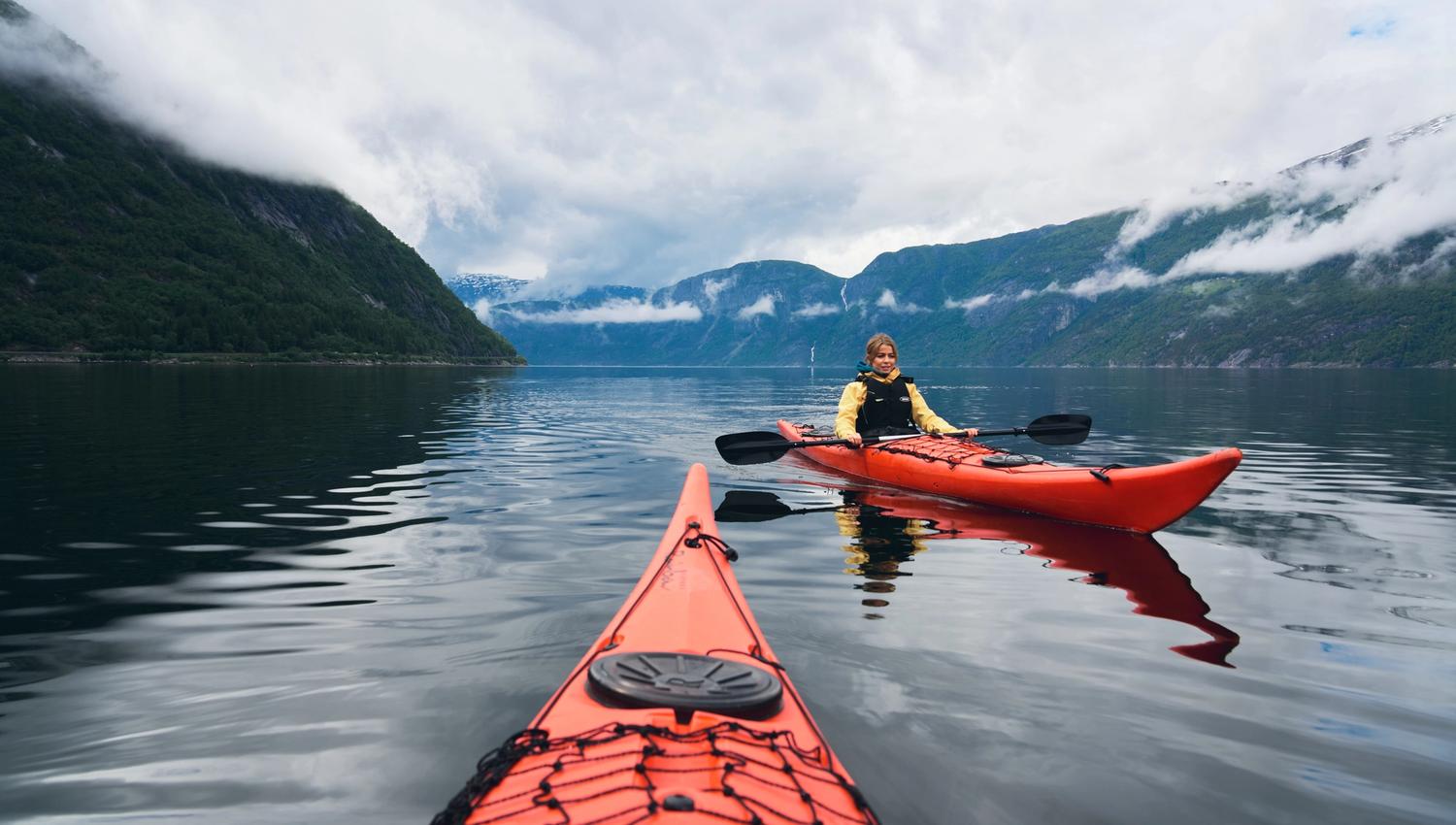 A woman in a red kayak with misty mountains in the background.