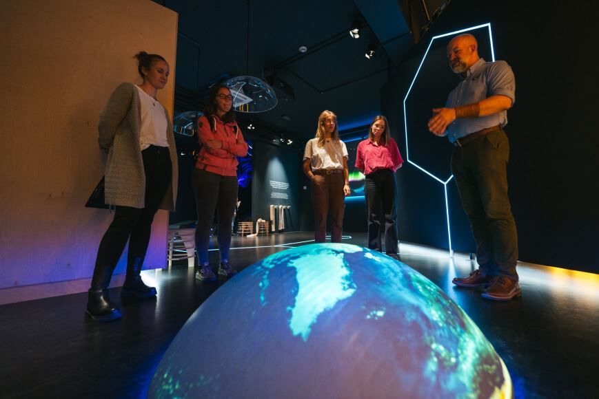 Fem personer rundt digital jordklode i mørklagt utstillingsrom.