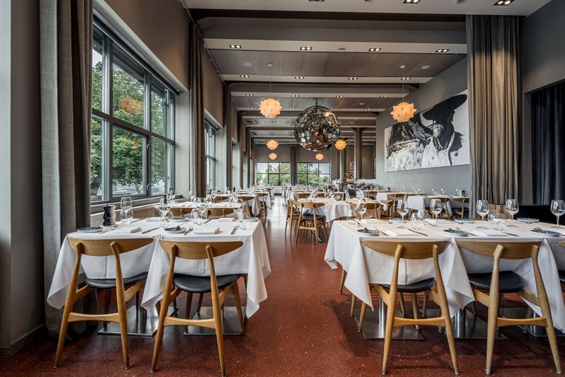 Spacious restaurant with neatly set tables, designer lighting and views through large windows.