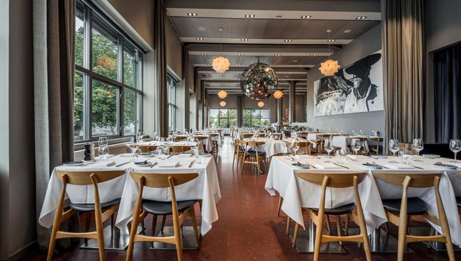 Spacious restaurant with neatly set tables, designer lighting and views through large windows.