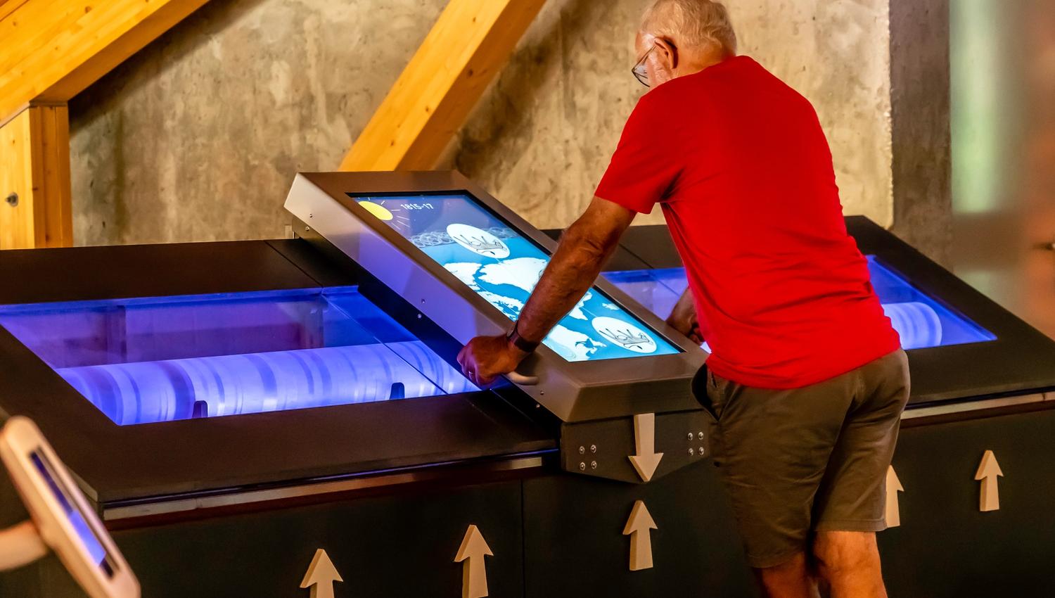 An older man is playing with an interactive exhibition piece.