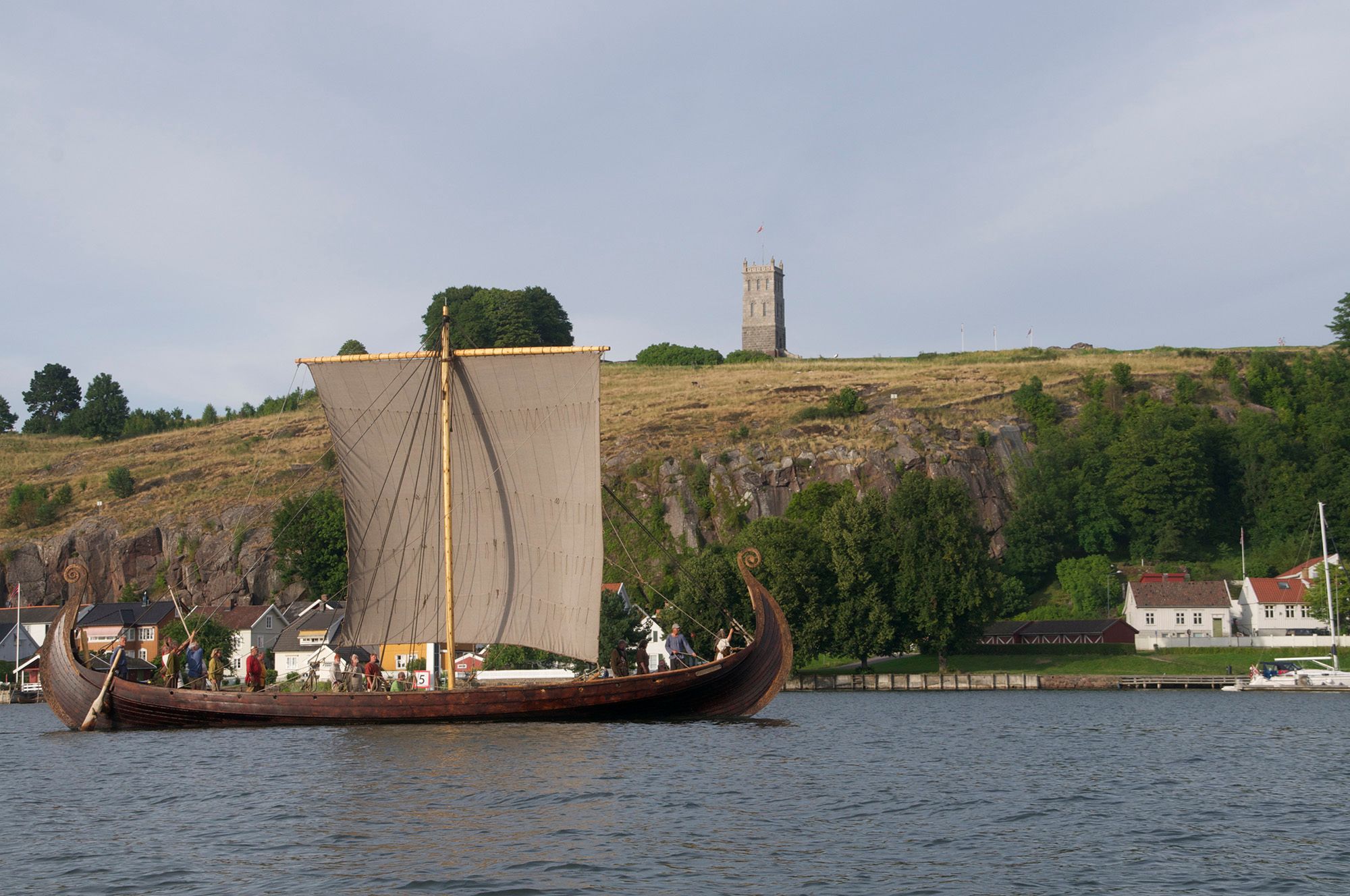 A large wooden ship with its sails up sails past with Slottsfjelltårnet in the background.