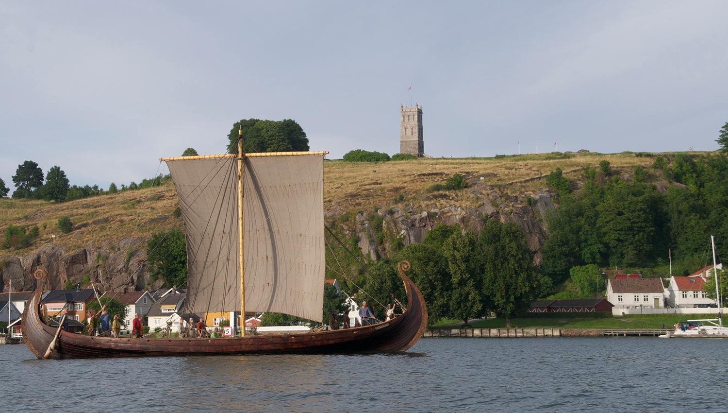 A large wooden ship with its sails up sails past with Slottsfjelltårnet in the background.