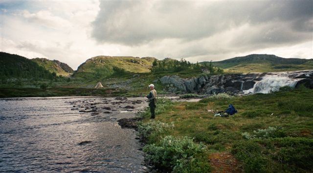 Angler fishing by a calm river and waterfall in the mountain landscape of Hardangervidda.
