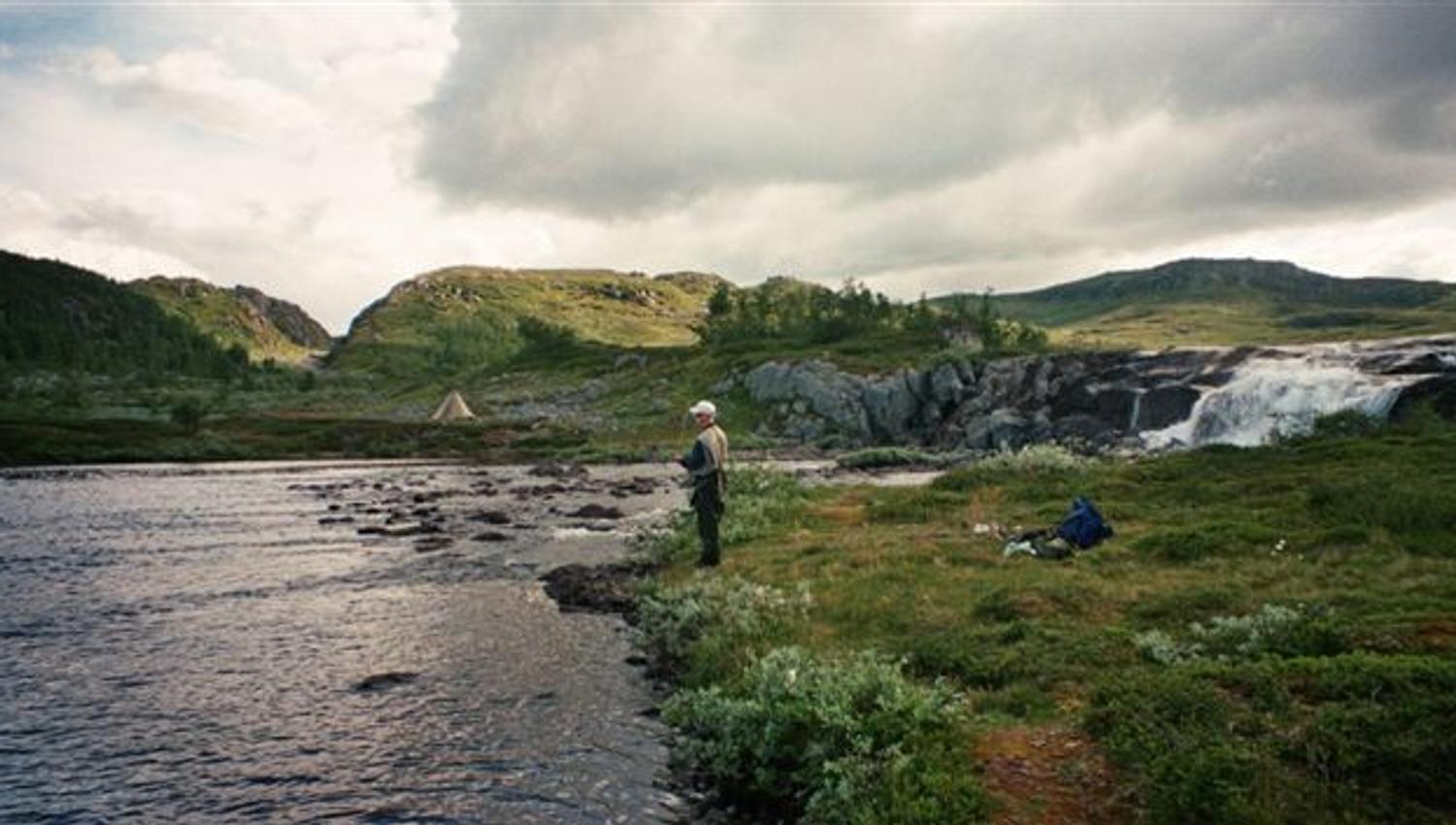 Angler fishing by a calm river and waterfall in the mountain landscape of Hardangervidda.