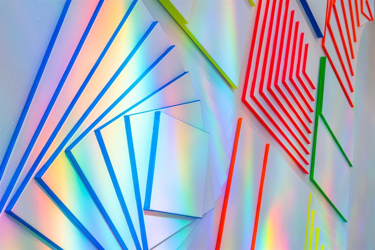 Kunstutstilling Kunstbanken - Fargerike geometriske kunstpaneler med lysrefleksjoner.