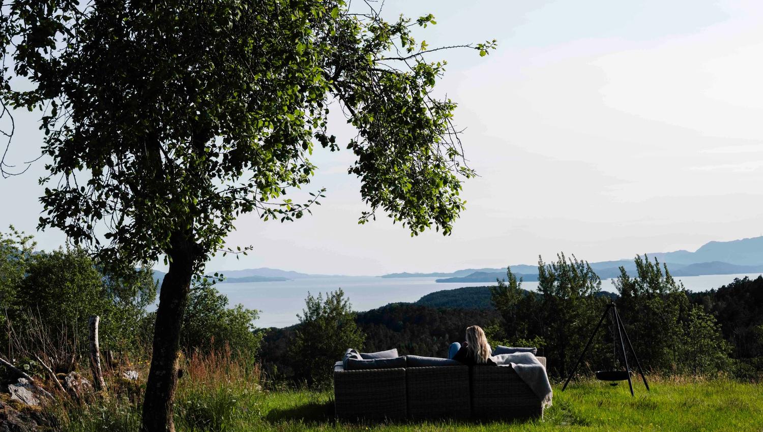 Person nyt utsikta frå utesofaen ved Stigen Fjordlodge i Hardanger.