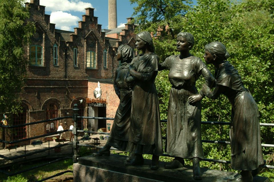 Statue av fire jenter med trær og bygning i bakgrunnen.