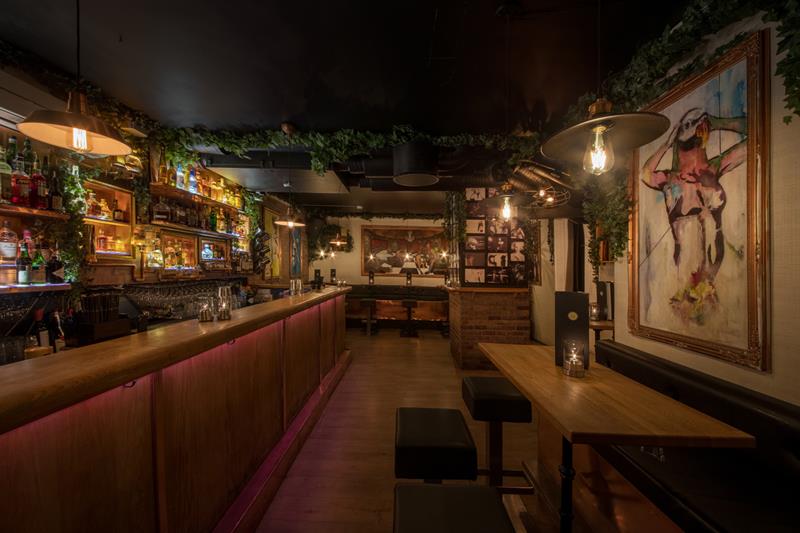 Interior: bar counter on the left side, a table, bar stools and a painting on the right.