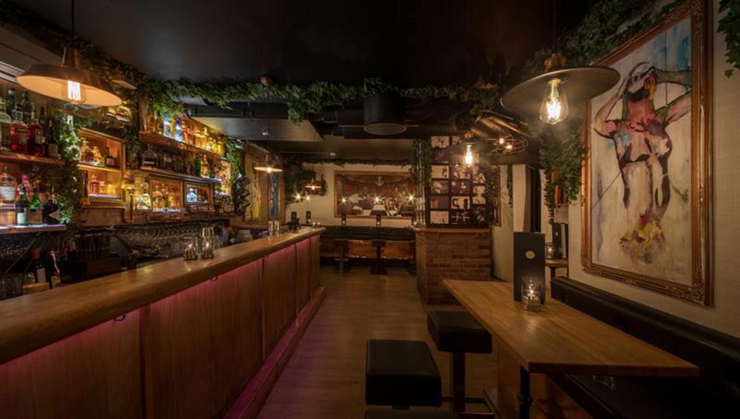 Interior: bar counter on the left side, a table, bar stools and a painting on the right.