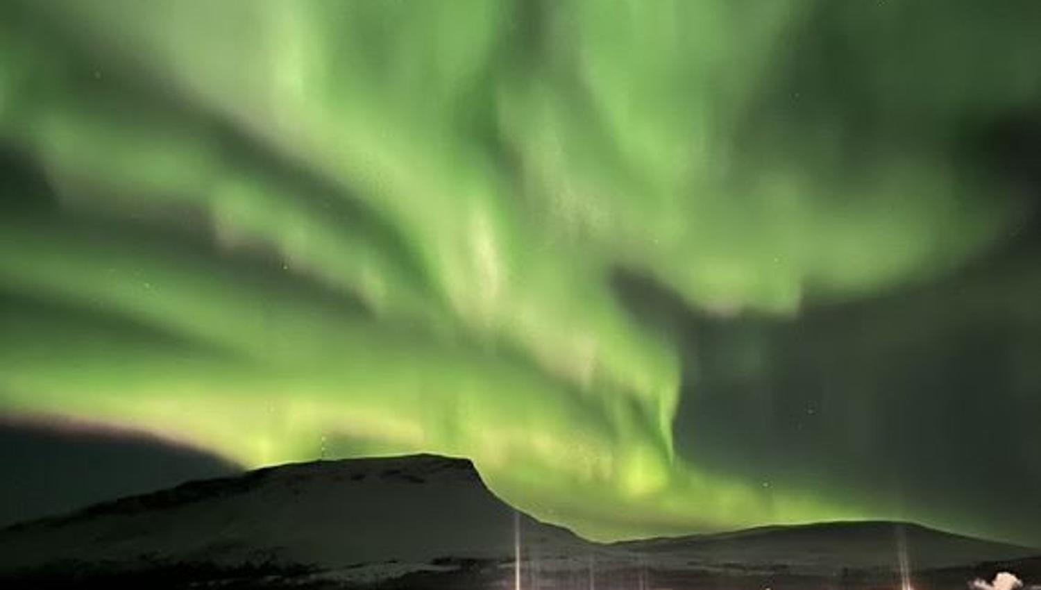 The Aurora Borealis covers the sky above a mountain