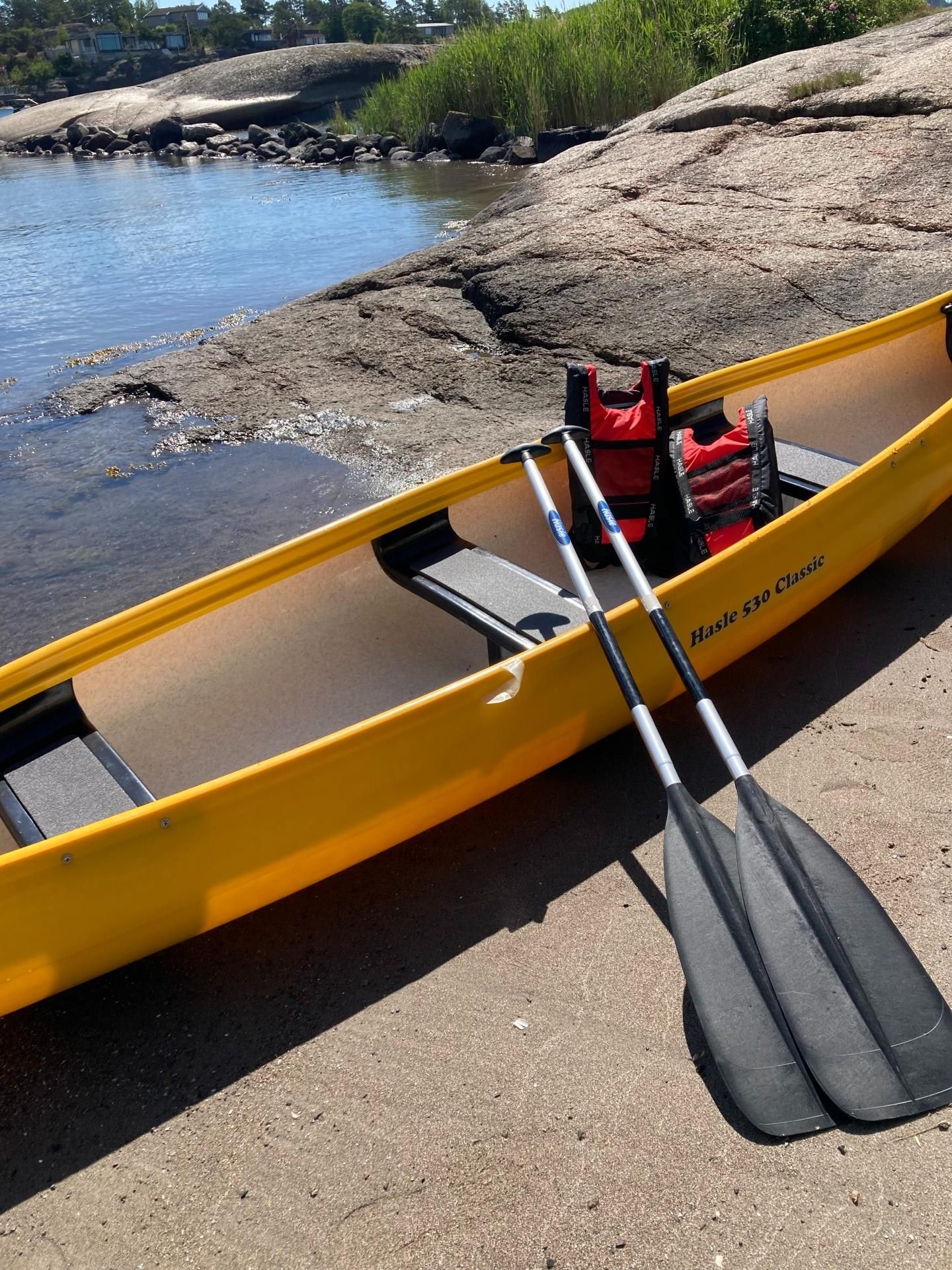 A yellow canoe with oars and vests on land