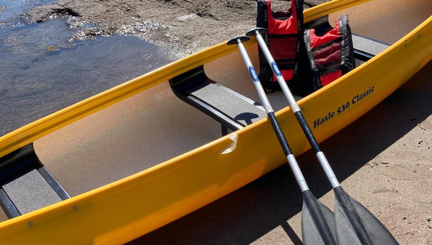 A yellow canoe with oars and vests on land