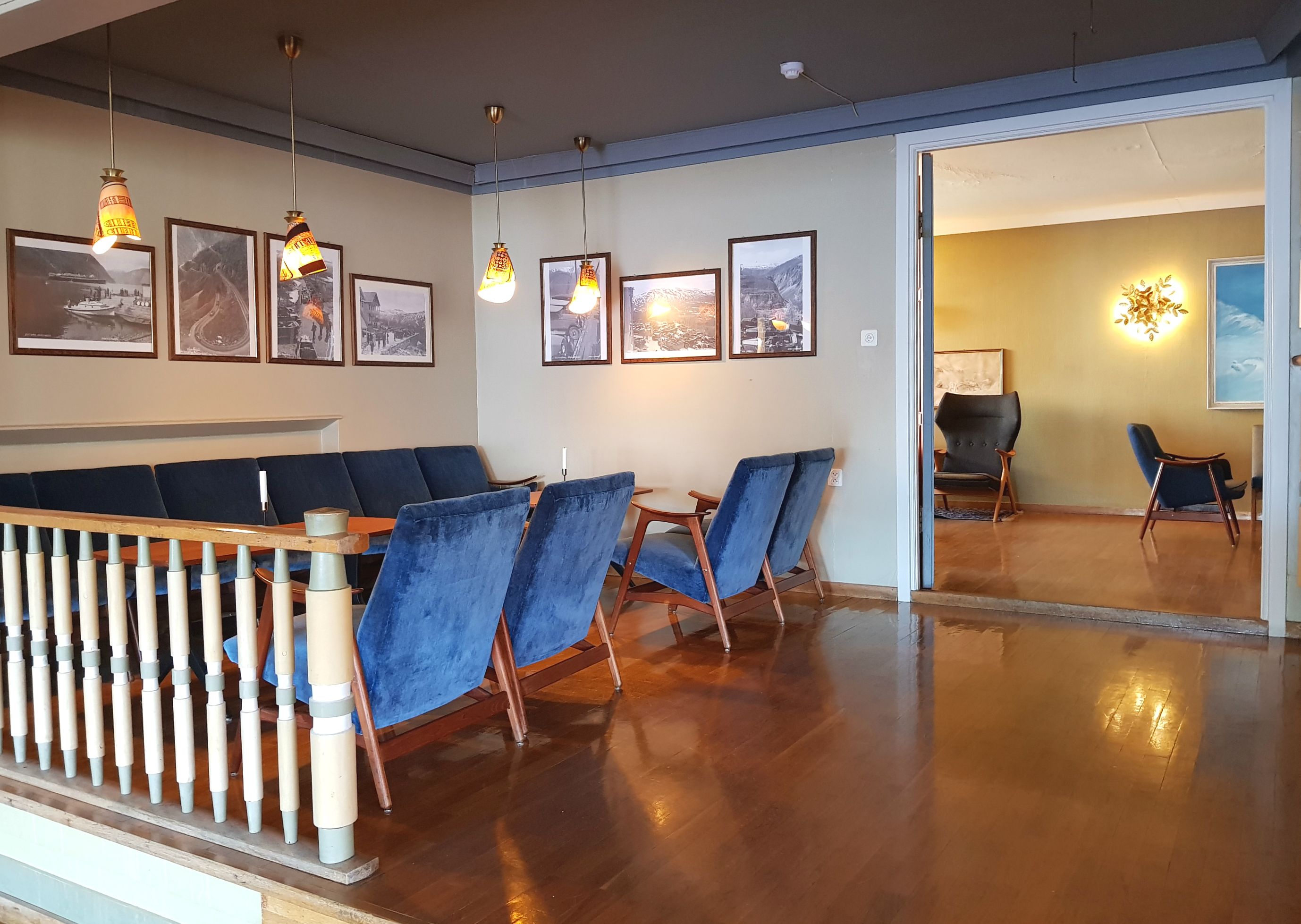 En sofa, noen stoler og et bord, med malerier hengende på veggene over.