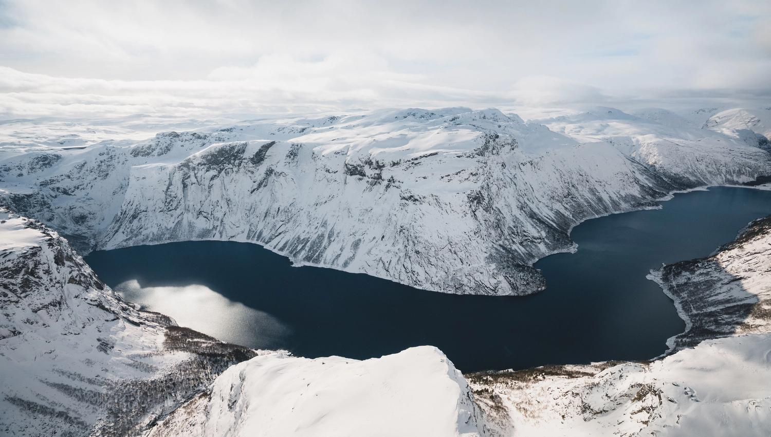 Oversiktsbilde over Hardangerfjorden med snøkledde fjell rundt.