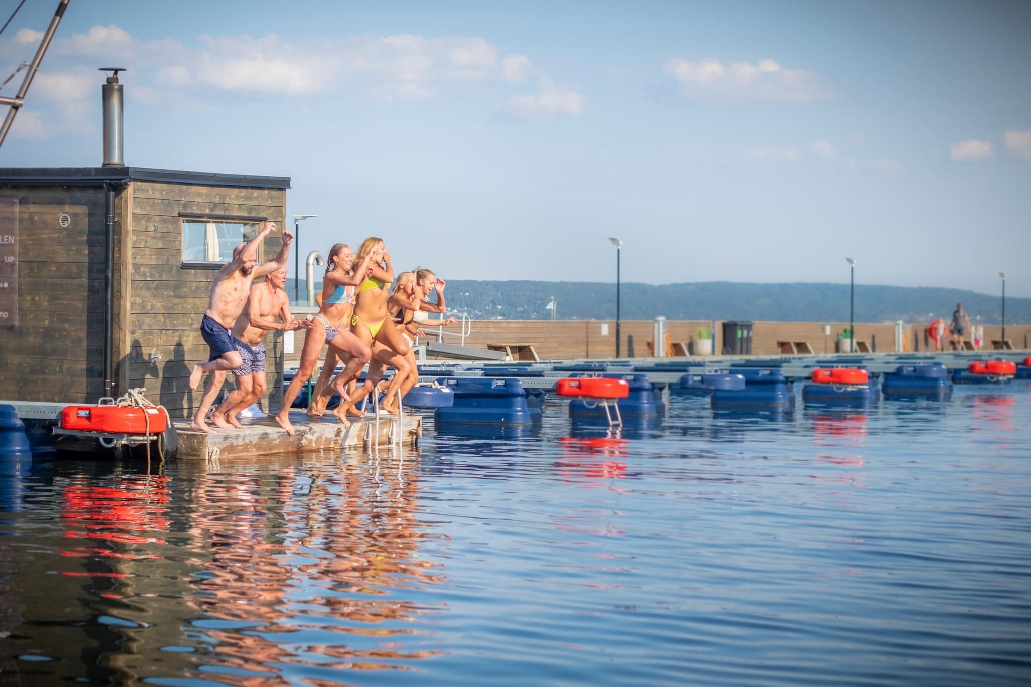 Gjeng gutter og jenter hopper i vannet fra badstueflåten Varm i Vollen