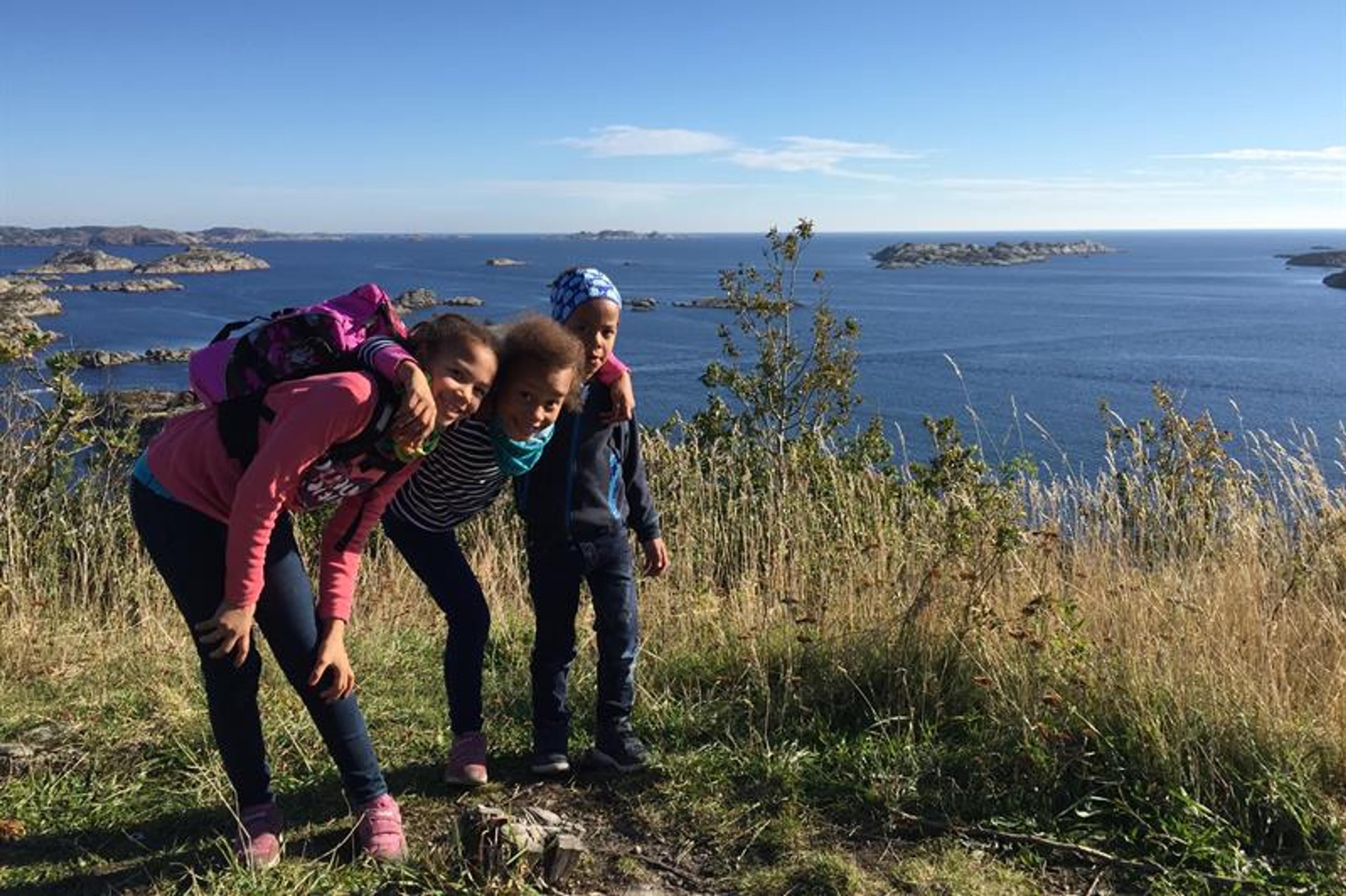 Tre barn på toppen av utsiktpunktet med havet bak seg og åpen himmel