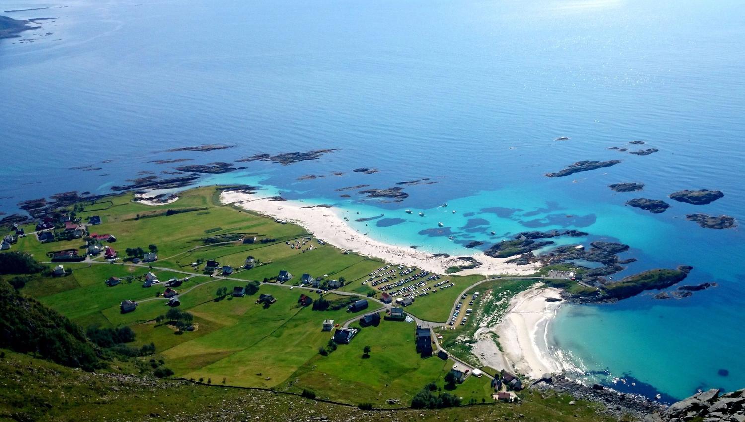 Grotlesanden. Aerial view of a green coastal village with roads and houses beside white-sand beaches and turquoise water with rocky islets..