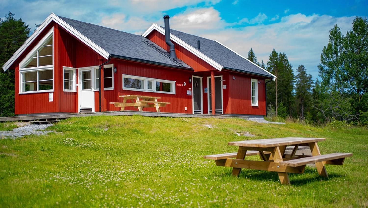 The red Østtorphytta. In the foreground – green grass and a picnic table. Photo.